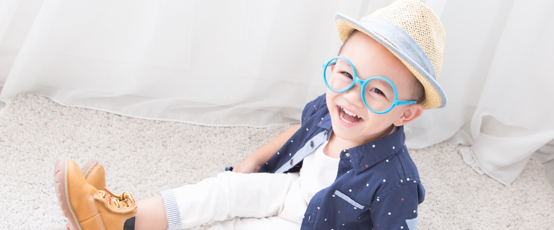 Ein kleiner Junge mit stylischem Hut und blauer übergroßer Sonnenbrille.