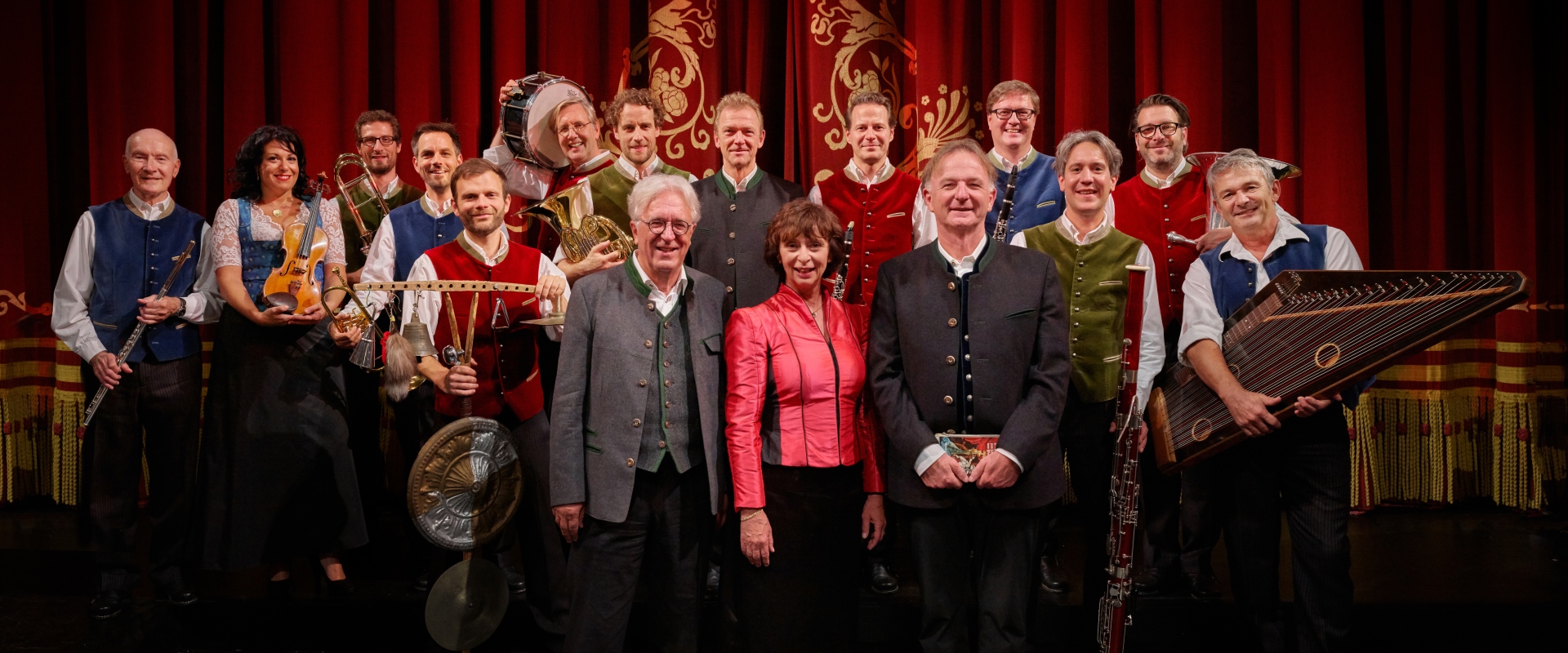 Das Ensemble von Opern auf Bayrisch vor einem roten Bühnenvorhang.