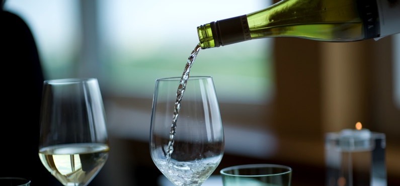 Weißwein wird in ein hohes Glas an einem schön gedeckten Tisch eingeschenkt.