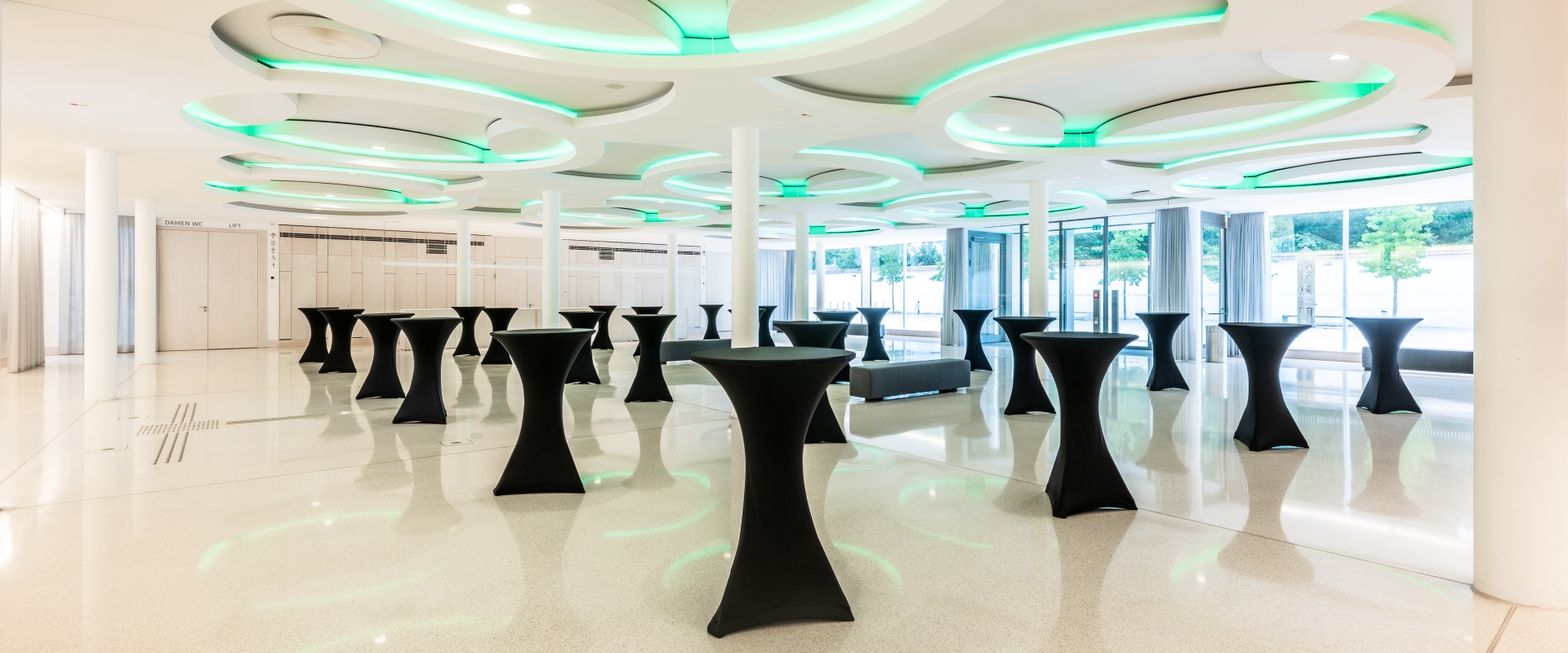Das Foyer Abends im Forum Altötting, mit Stehtischen, die schwarze Hussen tragen und grüner Beleuchtung.