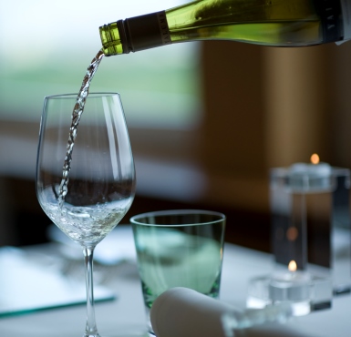 Weißwein wird in ein hohes Glas an einem schön gedeckten Tisch eingeschenkt.