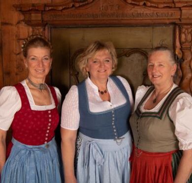 Drei Frauen in Dirndl stehen vor einer Holzwand