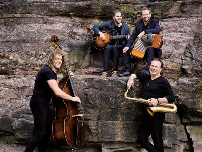 Vier Männer mit Instrumenten sitzen auf einem großen Felsen.
