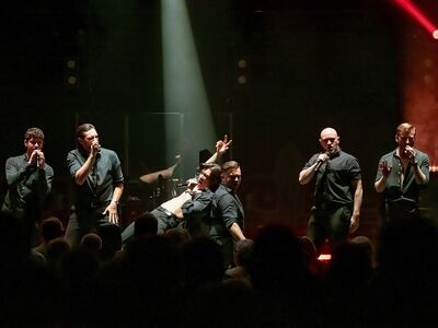 12 Sänger in schwarzen Anzügen auf der Bühne.