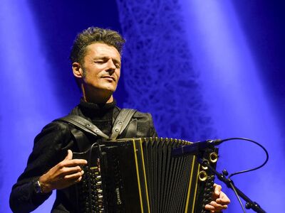 Herbert Pixner, Forum, Altötting, Bild Sylvia Größwang Ein Mann mit Akkordeon vor einem blauen Hintergrund.