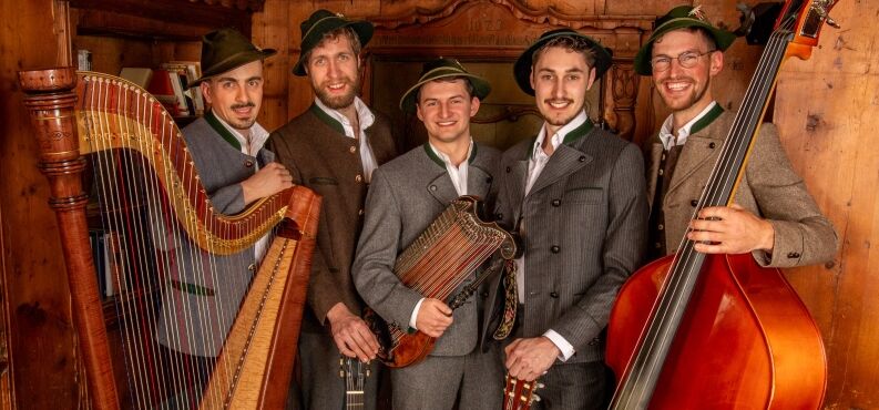 Damals an Weihnachten, Harald Krassnitzer, Forum, Altötting Foto Veranstalter Fünf Musiker in Tracht stehen mit ihren Instrumenten vor einer Holzwand.