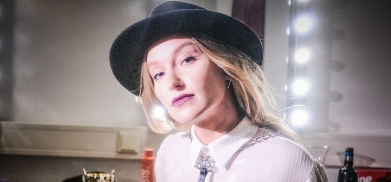 Malarina, KULTUR+KONGRESS FORUM ALTÖTTING, Foto: Christopher Glanzl Die junge Kabarettistin Malarina posiert mit Hut vor einem Garderobenspiegel.