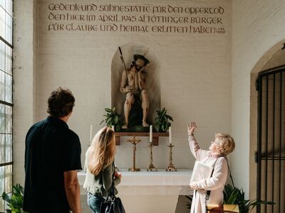 Stadtführung Altöting Heimat.Stadt.Widerstand, Foto Tourismusverband Inn-Salzach Die Stadtführerin erläutert das Gedenkmal zu den Altöttinger Bürgermorden.