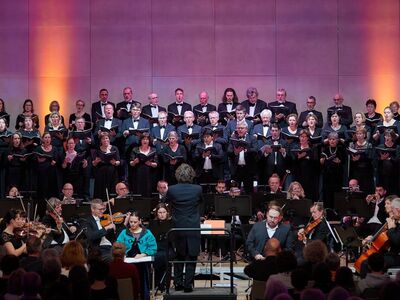 Euregio Oratorienchor, André Gold, Bad Reichenhaller Sinfonieorchester, Forum Altötting, Bild Irmi Mayer Musiker und Orchester stehen vor einer rot beleuchteten Wand.