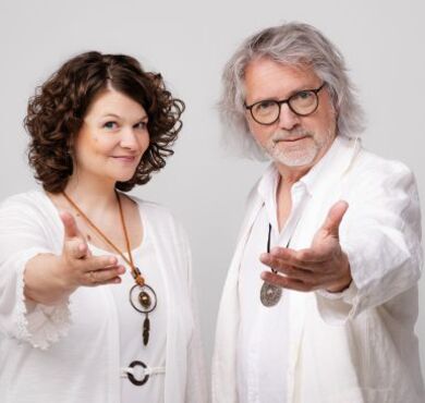 Das Kabarett-Duo Petzenhauser & Wählt in weißen Outfits bei Yoga-Posen mit esoterischem Schmuck und humorvoll übertriebenen Handbewegungen.