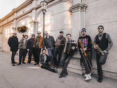 Zehn Musiker lehnen an einer Wand und haben Instrumente in der Hand.
