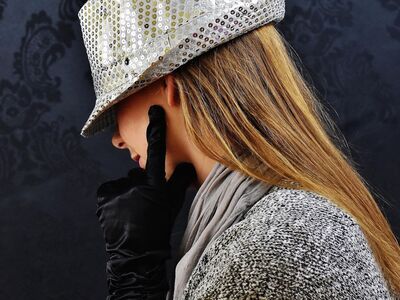 Eine junge Frau mit silbernem Hut und schwarzen Handschuhen ist nur von der Seite zu sehen.