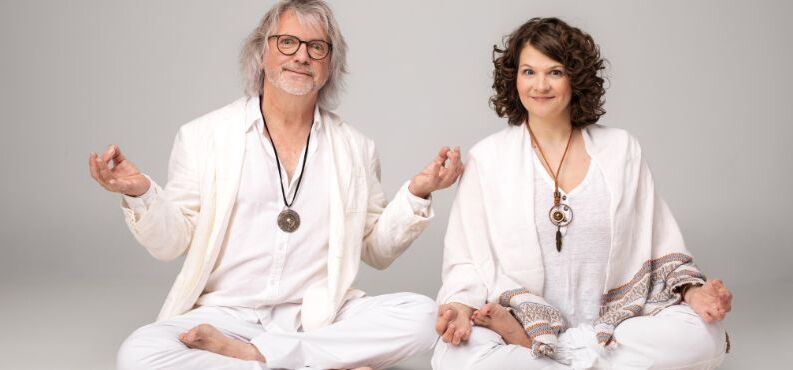 Das Kabarett-Duo Petzenhauser & Wählt in weißen Outfits bei Yoga-Posen mit esoterischem Schmuck und humorvoll übertriebenen Handbewegungen.