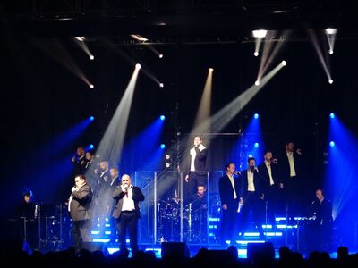 12 Sänger in schwarzen Anzügen auf der Bühne.