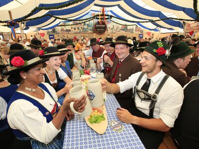 Menschen in Tracht sitzen in einem Zelt und halten Bierkrüge in der Hand.
