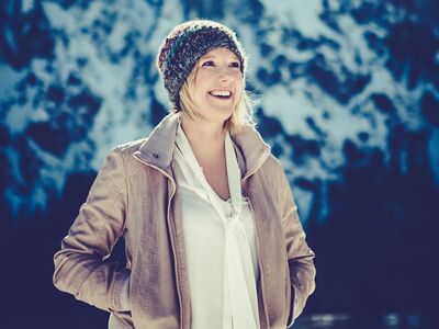Claudia Koreck, Weihnachtskonzert, Forum Altötting, Bild Lena Semmelroggen Eine Frau mit Jacke und Mütze in einer Landschaft mit Schnee und Sonne.