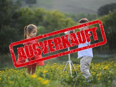 Zwei Kinder in modischen Kleidern stehen auf einer Wiese.