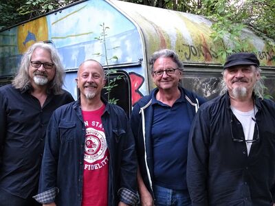 Vier ältere Männer stehen vor einem bunt bemalten Bauwagen.