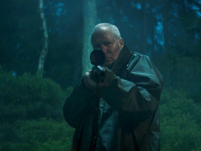 Der Schauspieler August Zirner hält eine Jagdwaffe direkt in die Kamera.