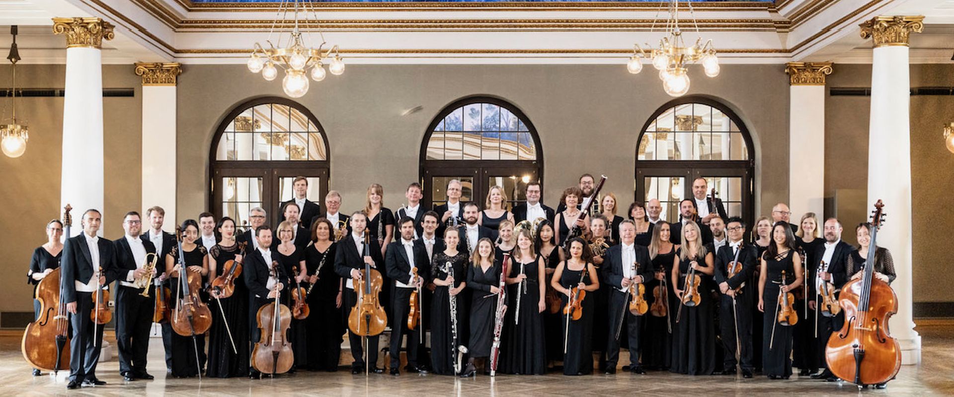 Das Ensemble der Münchner Symphoniker posiert in einem Prunkvollen Saal.