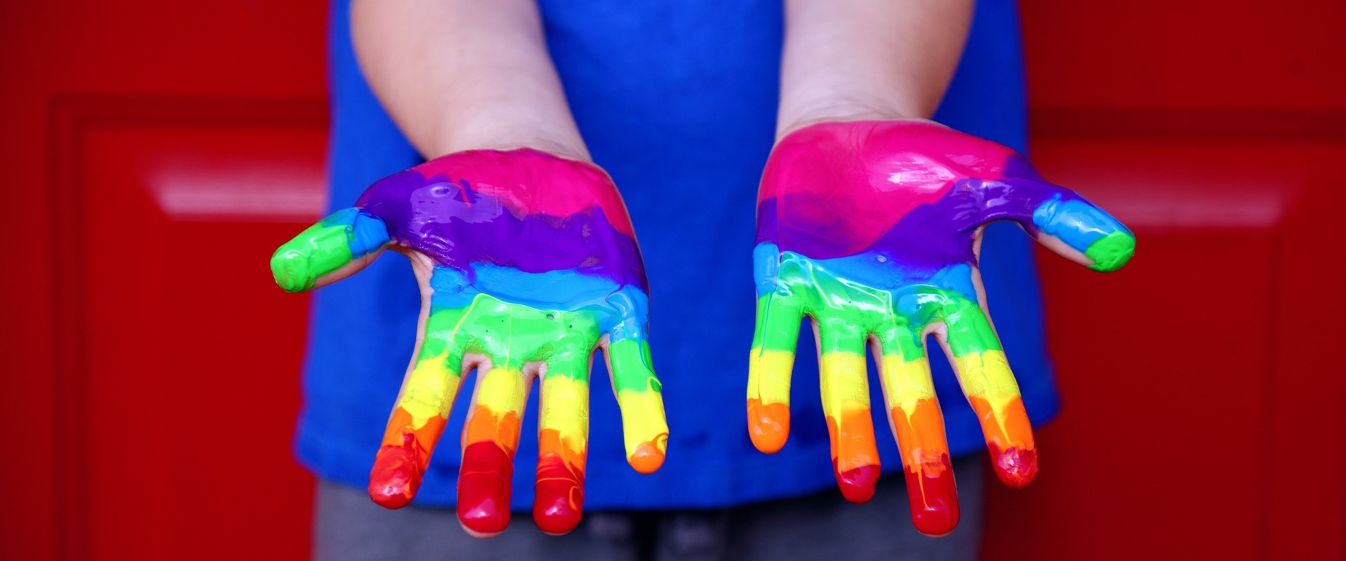 Ein Kind hat mit Fingerfarbe einen Regenbogen auf die Hände gemalt.