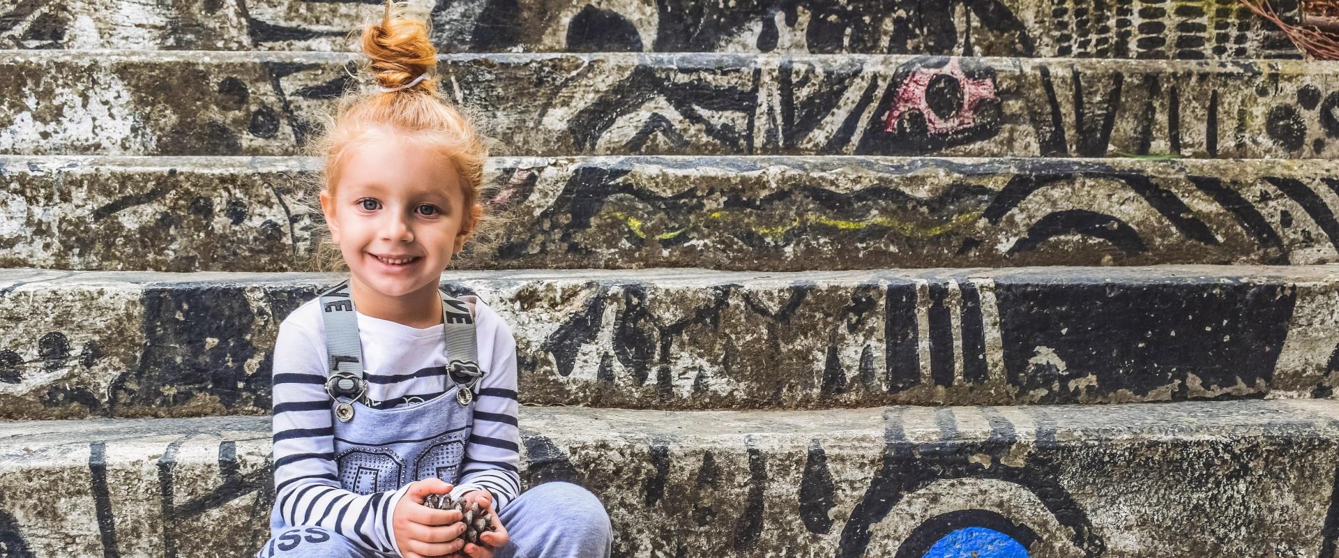 Ein kleines Mädchen sitzt vor einem Hintergrund mit viel Graffiti.