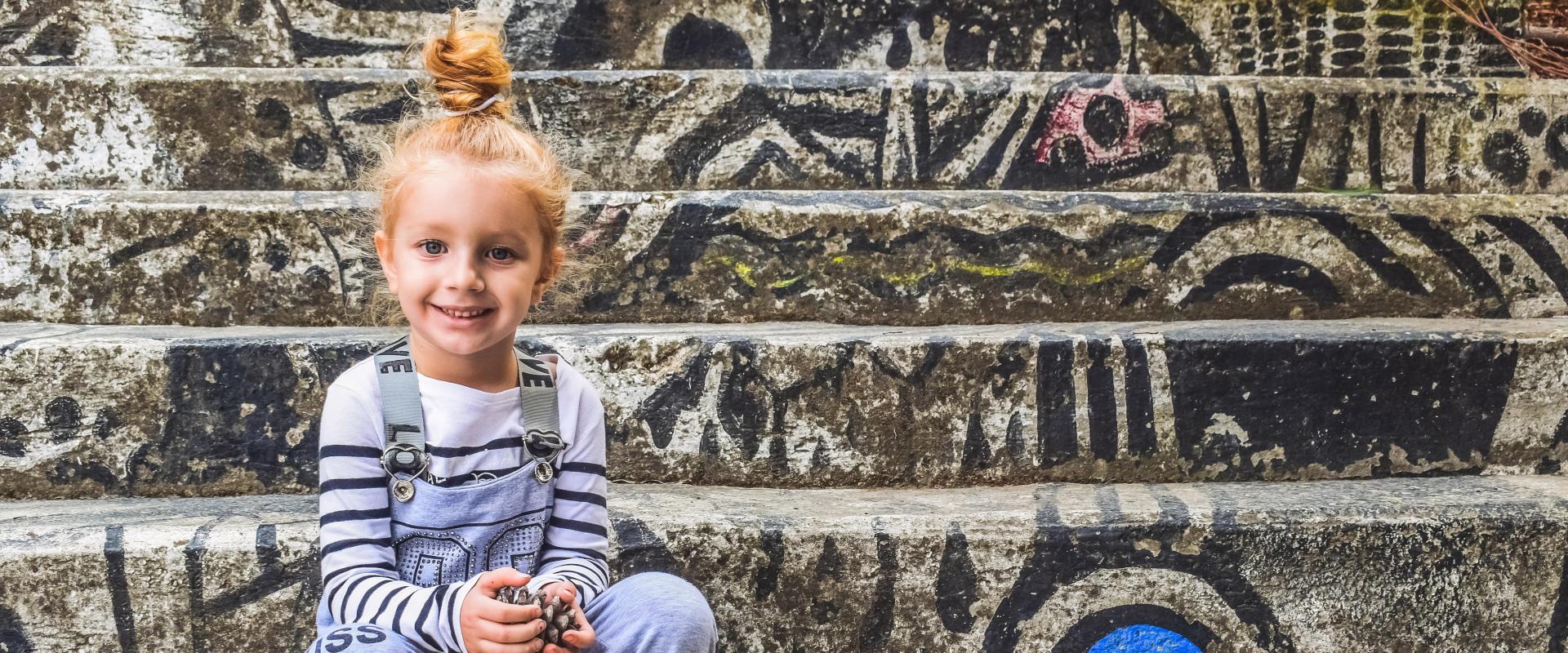 Kleines Mädchen sitzt auf einer Treppe mit vielen Graffitis.