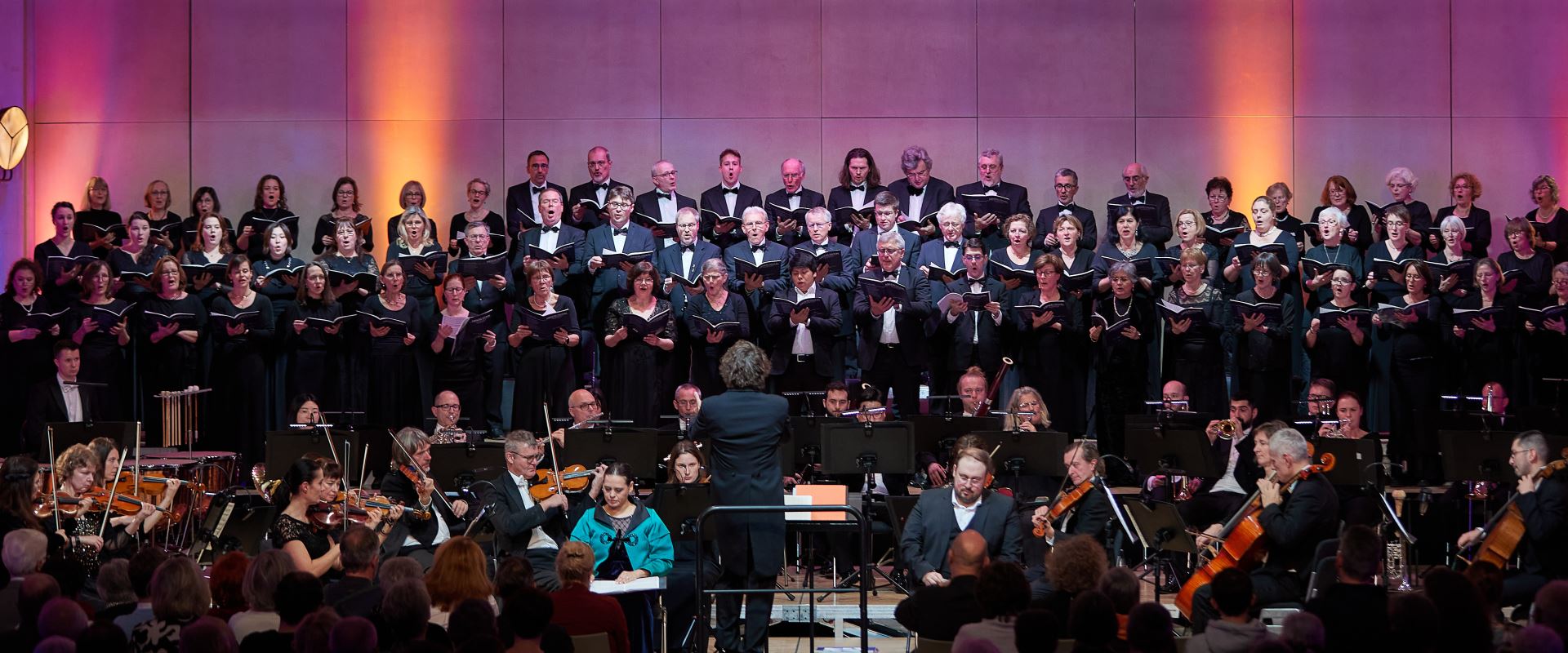 Musiker und Orchester stehen vor einer rot beleuchteten Wand.