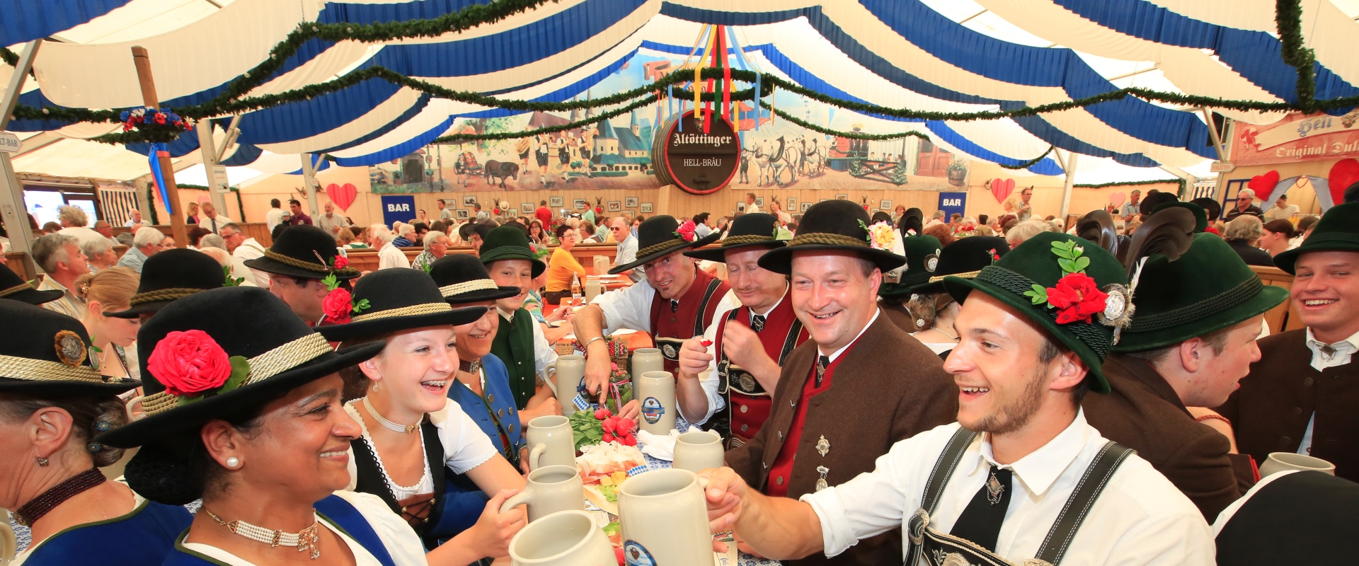 Menschen in Tracht sitzen in einem Zelt und halten Bierkrüge in der Hand.