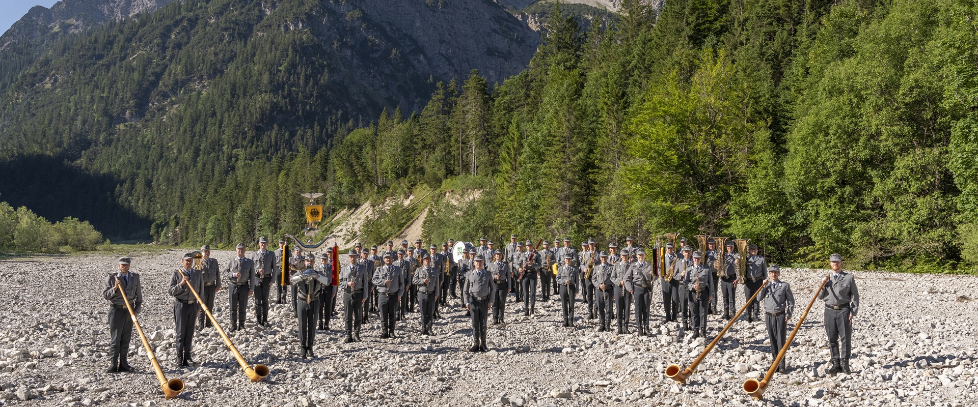 Musiker in Uniform vor Bergkulisse.