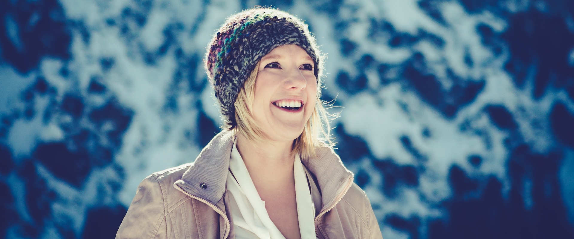 Eine Frau mit Jacke und Mütze in einer Landschaft mit Schnee und Sonne.