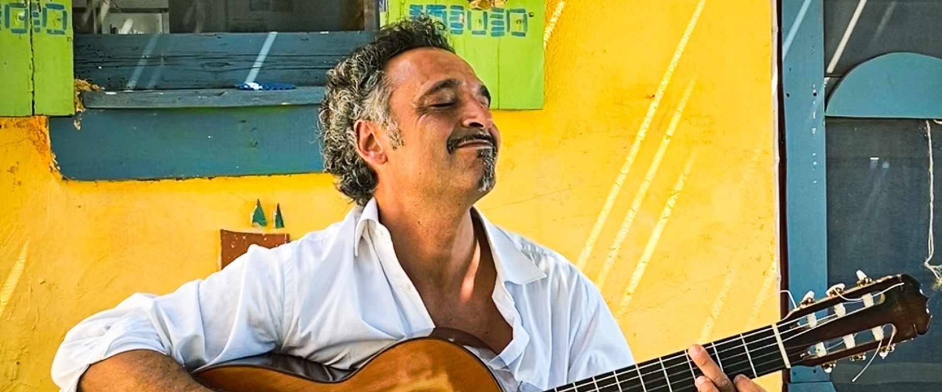 Ein Mann sitzt mit einer Gitarre vor eine bunten Hauswand.