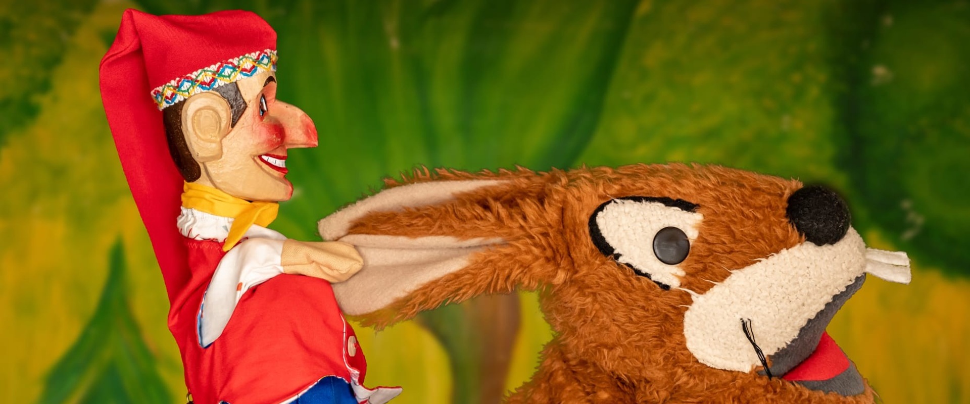 Holzpuppe Kasperl und ein Stoffhase auf der Puppenbühne.