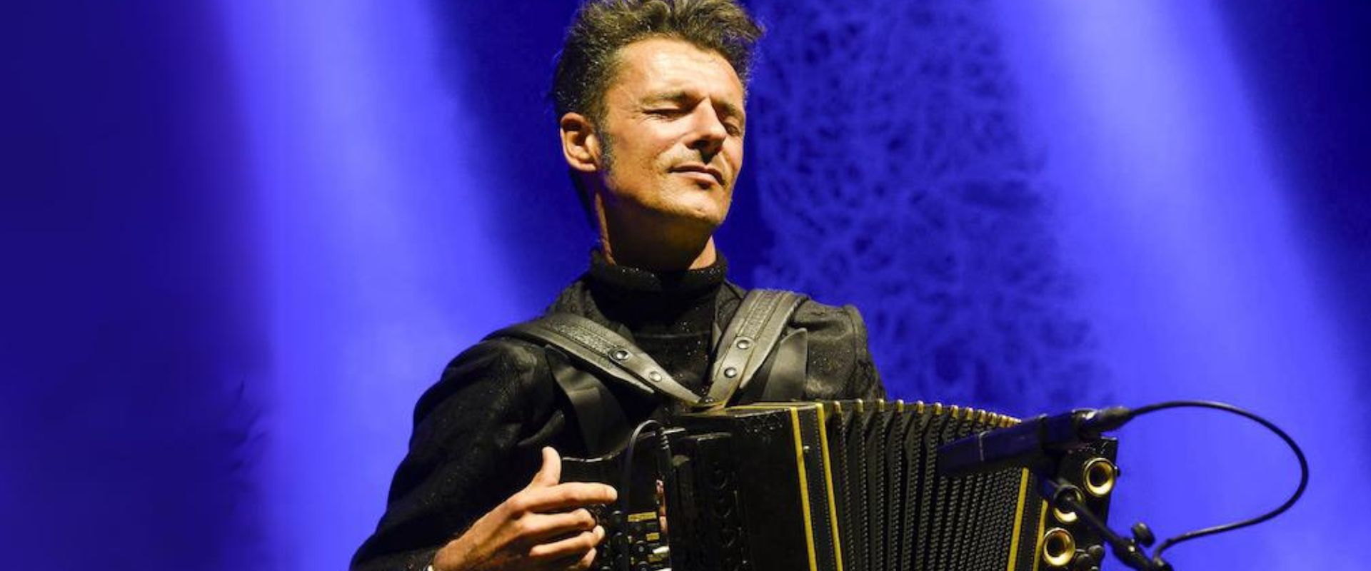 Ein Mann mit Akkordeon vor einem blauen Hintergrund.