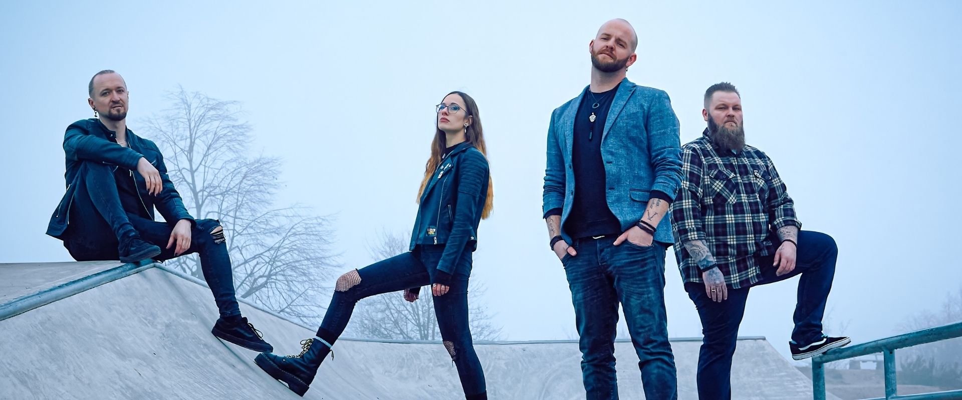 Drei Männer und eine Frau in dunkler Bekleidung stehen nebeneinander.