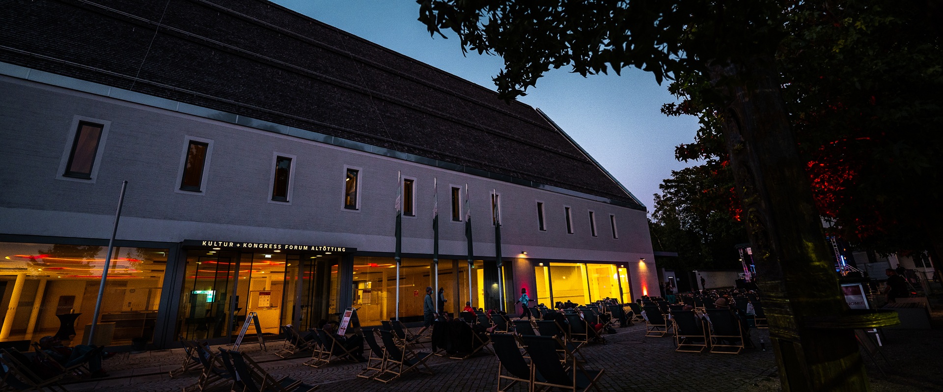Menschen sitzen auf Liegestühlen am Abend vor einem Gebäude.