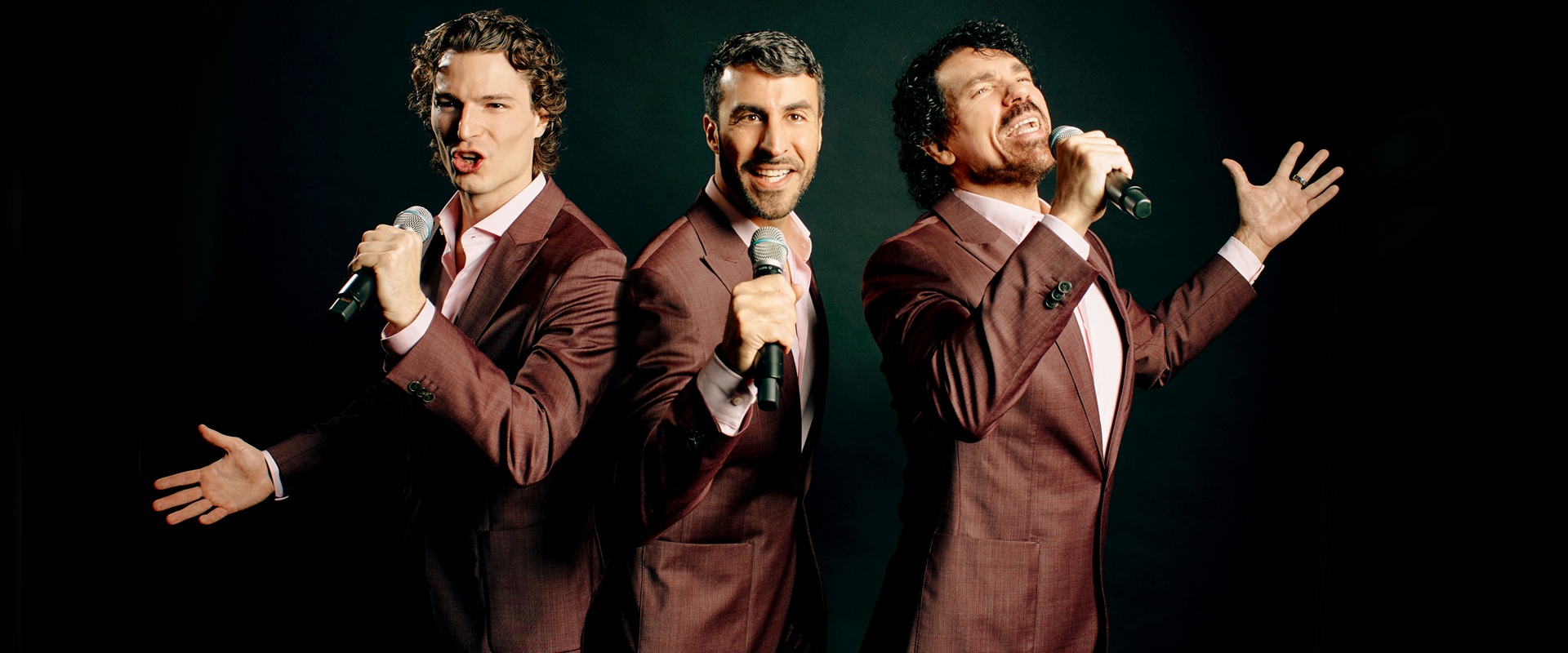 Drei  Männer in braunen Anzügen singen in ihre Mikrofone.