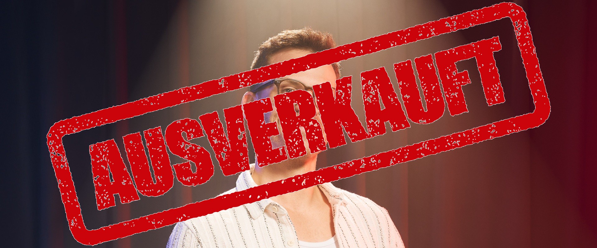 Ein Mann mit kurzärmeligem Hemd steht vor einem roten Vorhang.