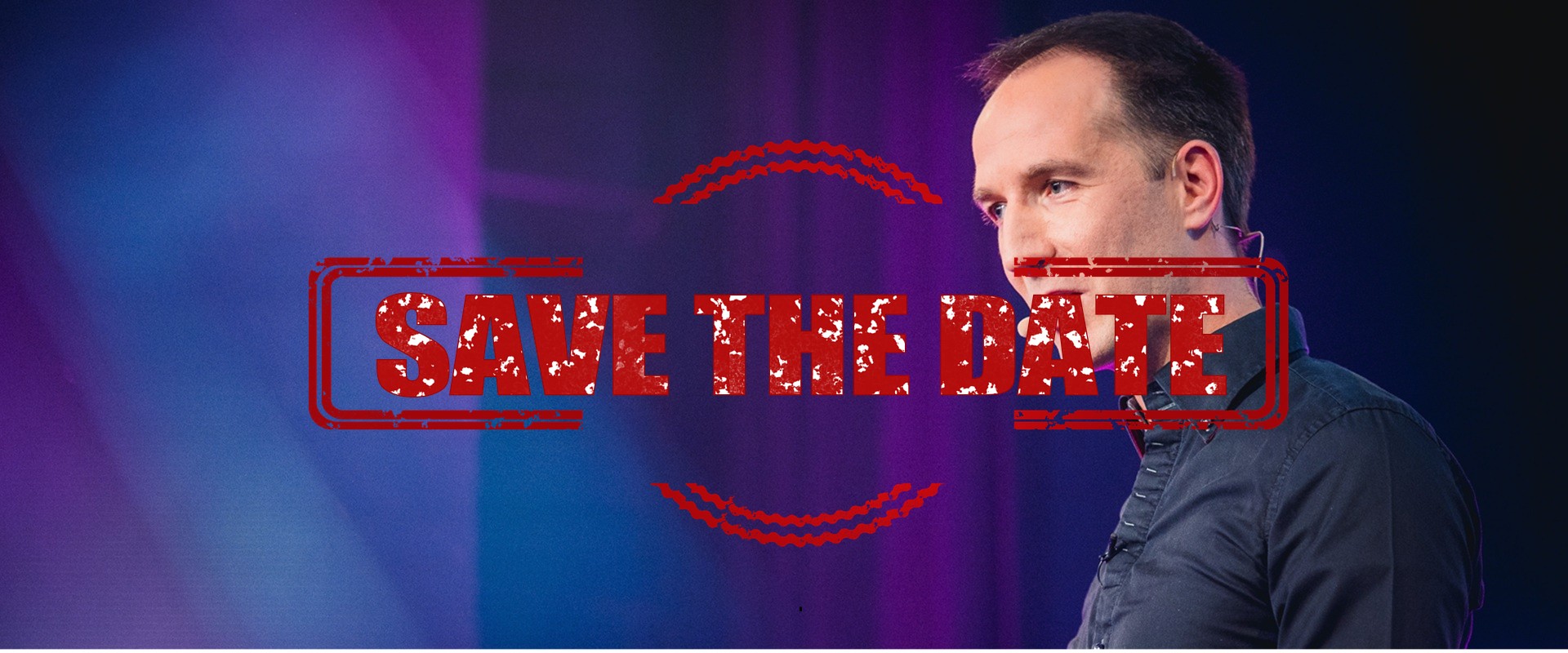 Ein Mann in dunklem Hemd vor einem bunten Hintergrund.