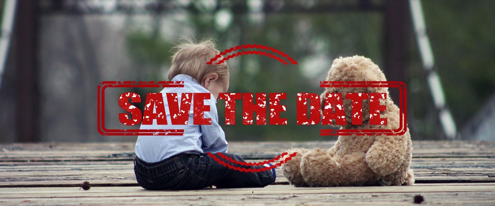 Ein kleiner Junge sitzt mit einem Teddybär auf einem Holzboden