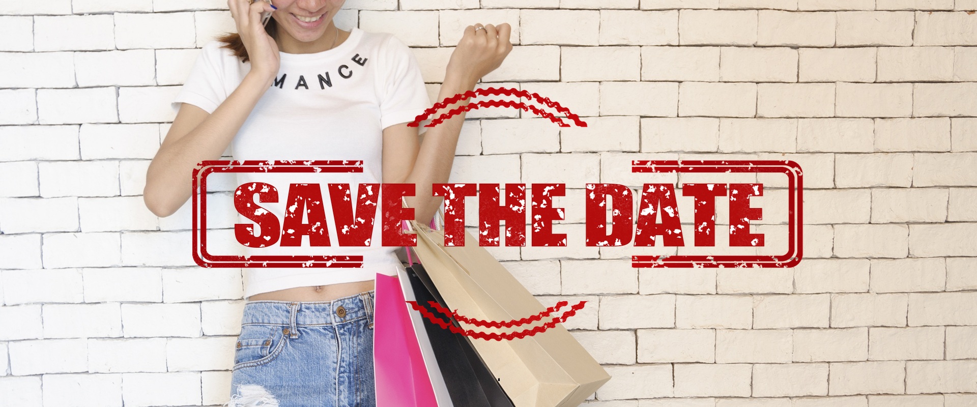 Eine junge Frau mit vielen Einkaufstaschen steht in Sommerkleidung an einer Wand und telefoniert.