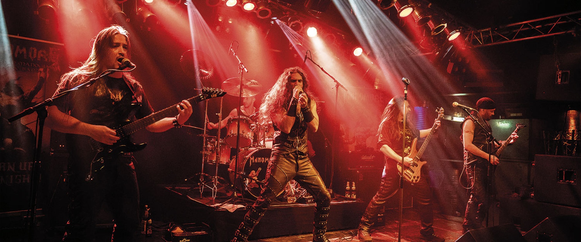Drei Männer mit Gitarren stehen auf der Bühne und schwingen die Haare zum Head Banging.