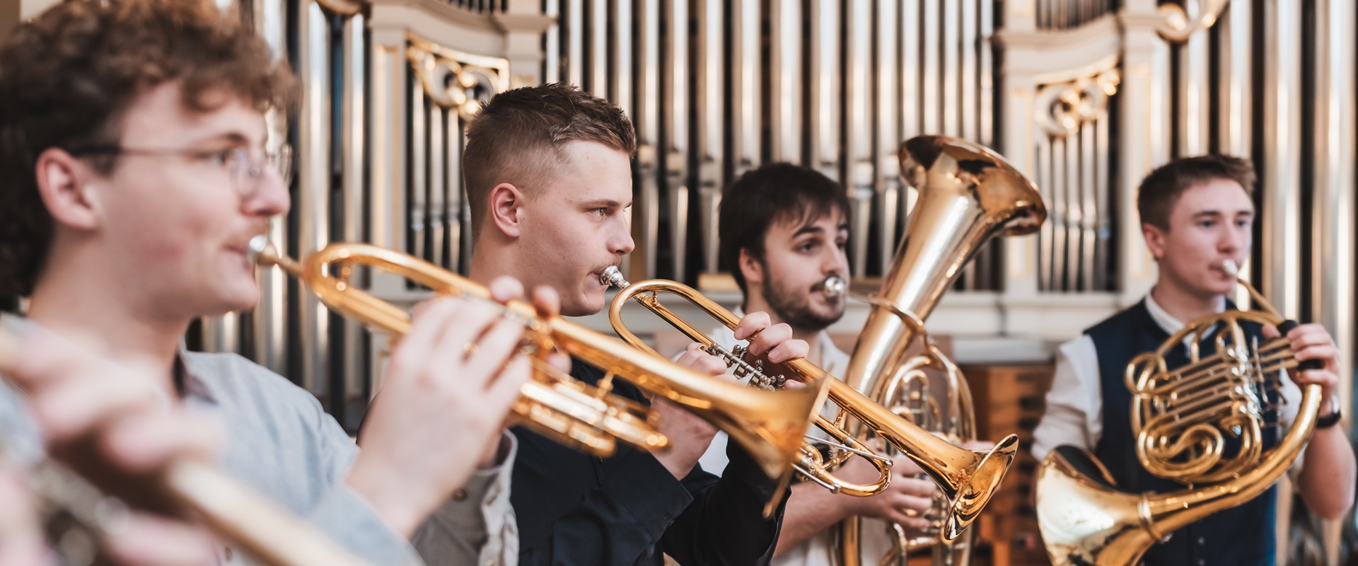 Vier junge Männer spielen auf verschiedenen Blasinstrumenten.