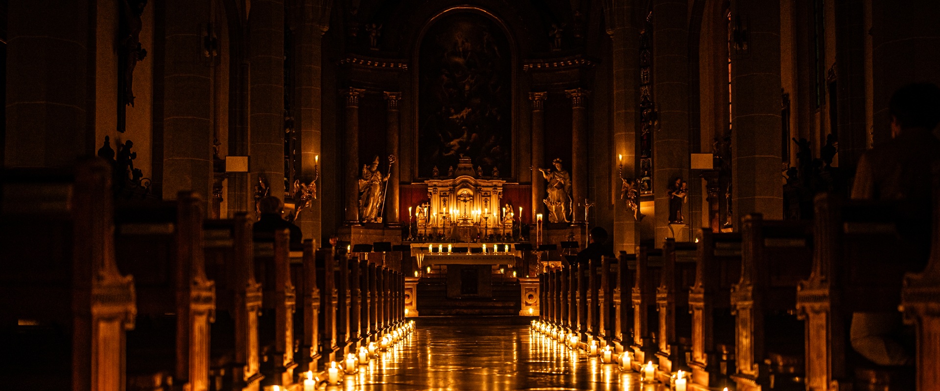 Ein Mittelgang in der einer Kirche nur mit Kerzen beleuchtet.