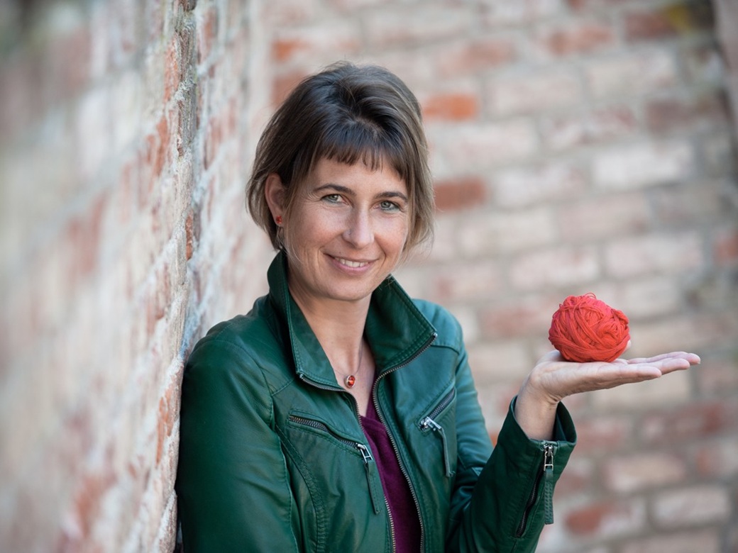 Senioren Daemmerschoppen, Stadtbuecherei Altoetting, Cordula Gernt, Bild Claudia Goeppert Eine Frau in grüner Jacke steht vor einer Steinmauer.