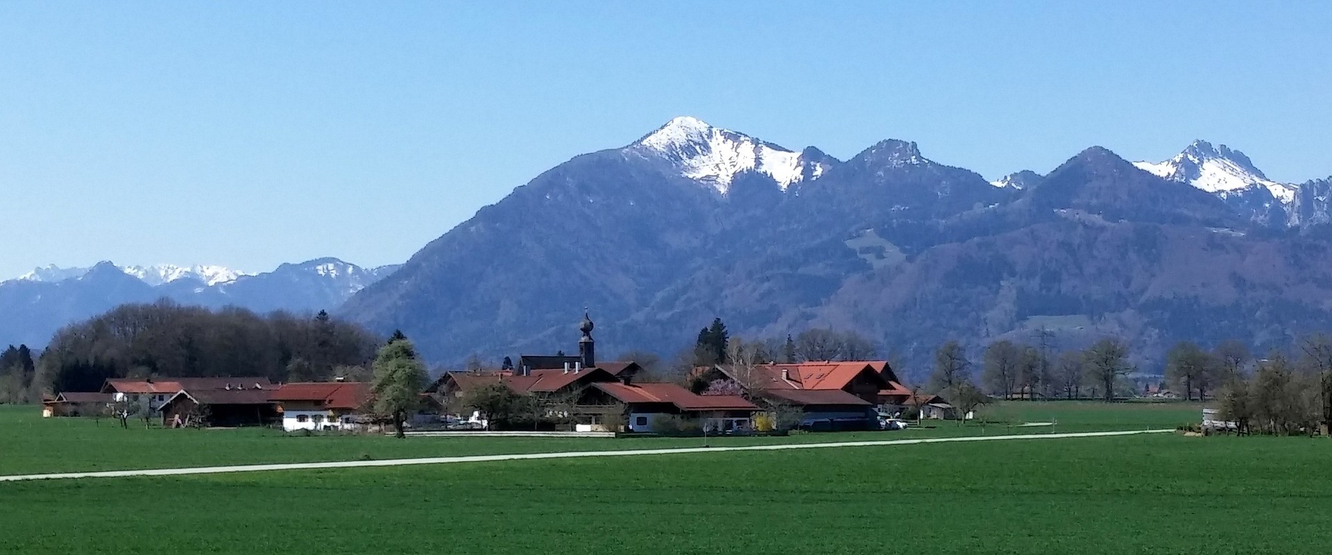 Ein Dorf im Chiemgau vor schneebedeckten Alpen.
