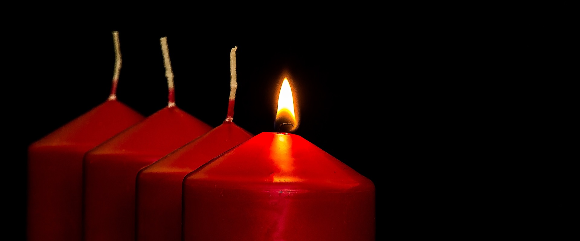 Die erste rote Kerze zu Advent brennt in einer Reihe von vier Kerzen.