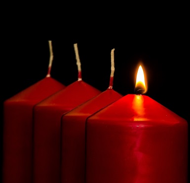 Die erste rote Kerze zu Advent brennt in einer Reihe von vier Kerzen.