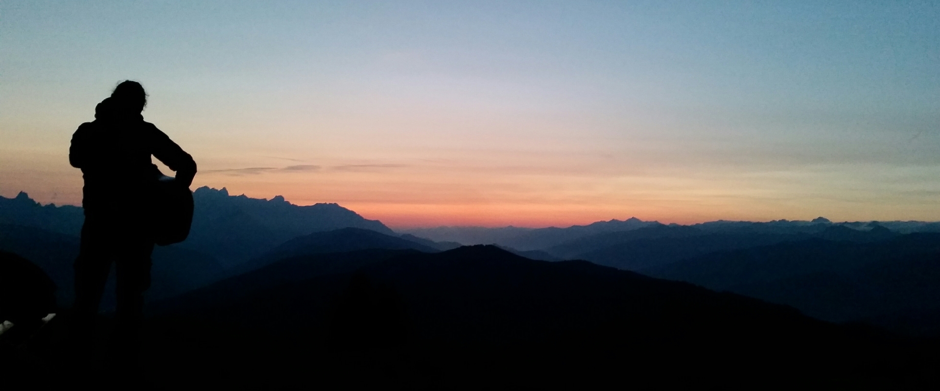 Alfons Hasenknopf steht auf einem Berg mit einer Gitarre und sieht in den Sonnenuntergang.