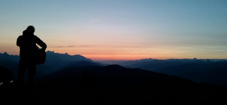 Alfons Hasenknopf steht auf einem Berg mit einer Gitarre und sieht in den Sonnenuntergang.